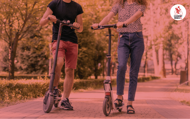 Dwoje dorosłych jedzie na hulajnogach elektrycznych po ścieżce w parku – rower czy hulajnoga do miasta