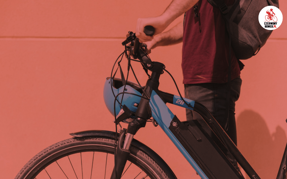 Mężczyzna prowadzący niebieski rower elektryczny z zamocowanym kaskiem, widok z boku – codzienne użytkowanie e-bike’a w mieście.